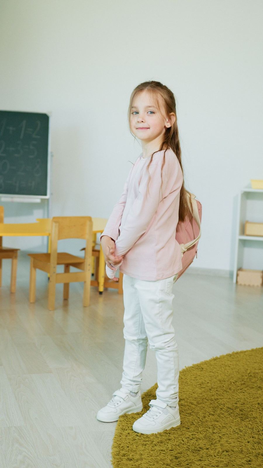 Young child wearing a backpack in a bright classroom