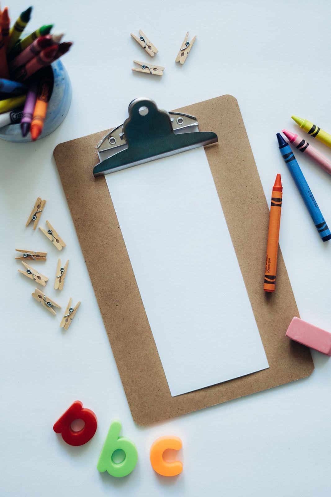 Clipboard surrounded by crayons, alphabet pieces, and small craft materials