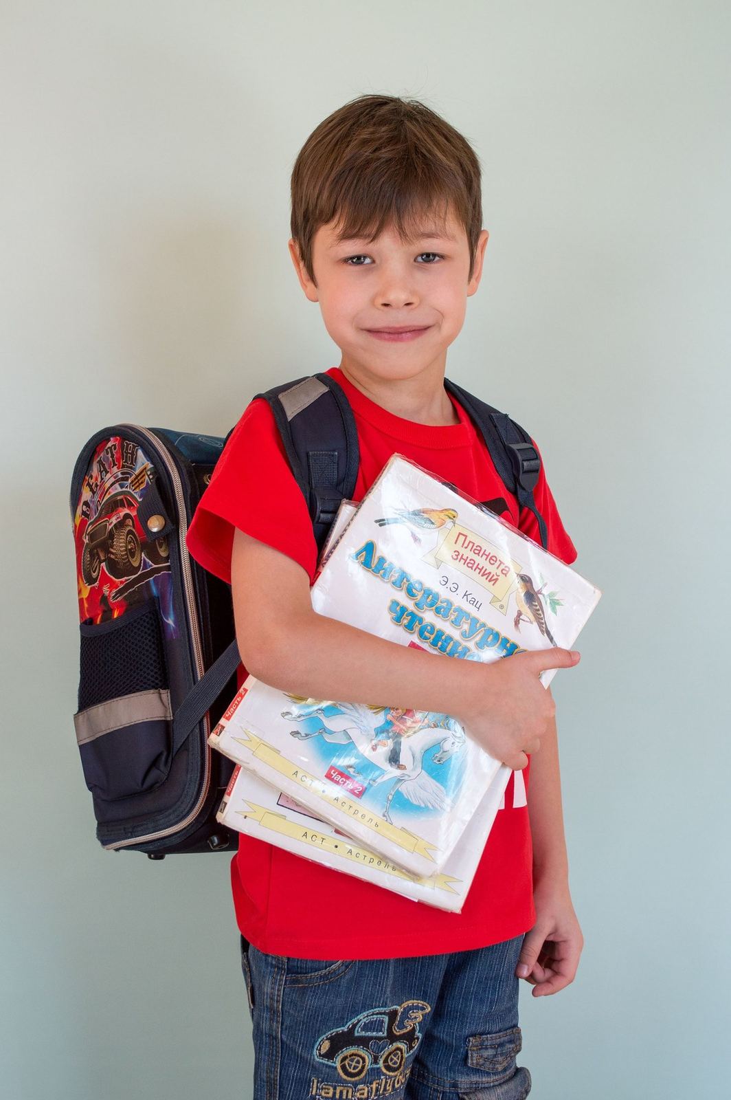 Young child carrying a backpack and holding several books