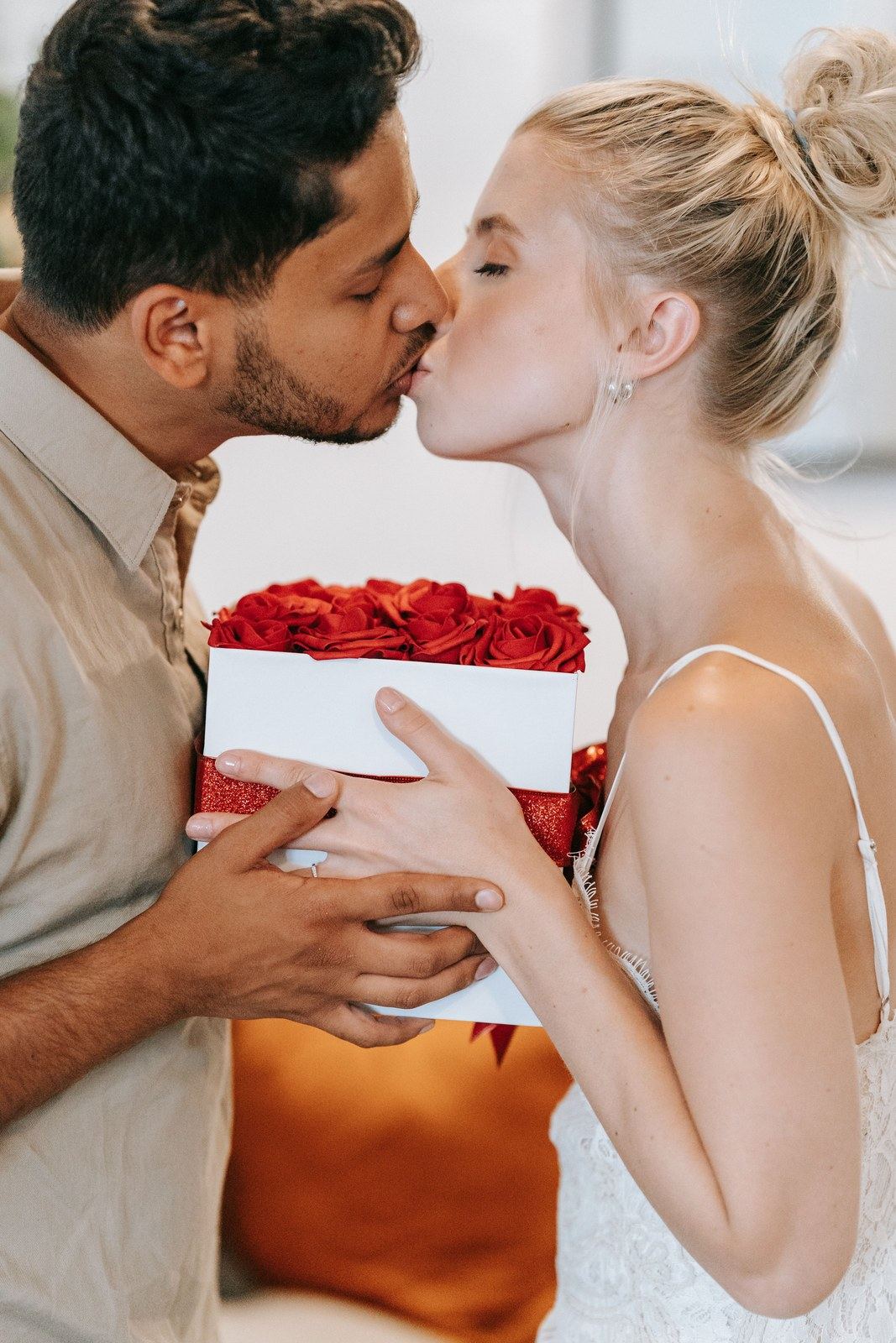 A couple kissing while holding a box filled with red roses