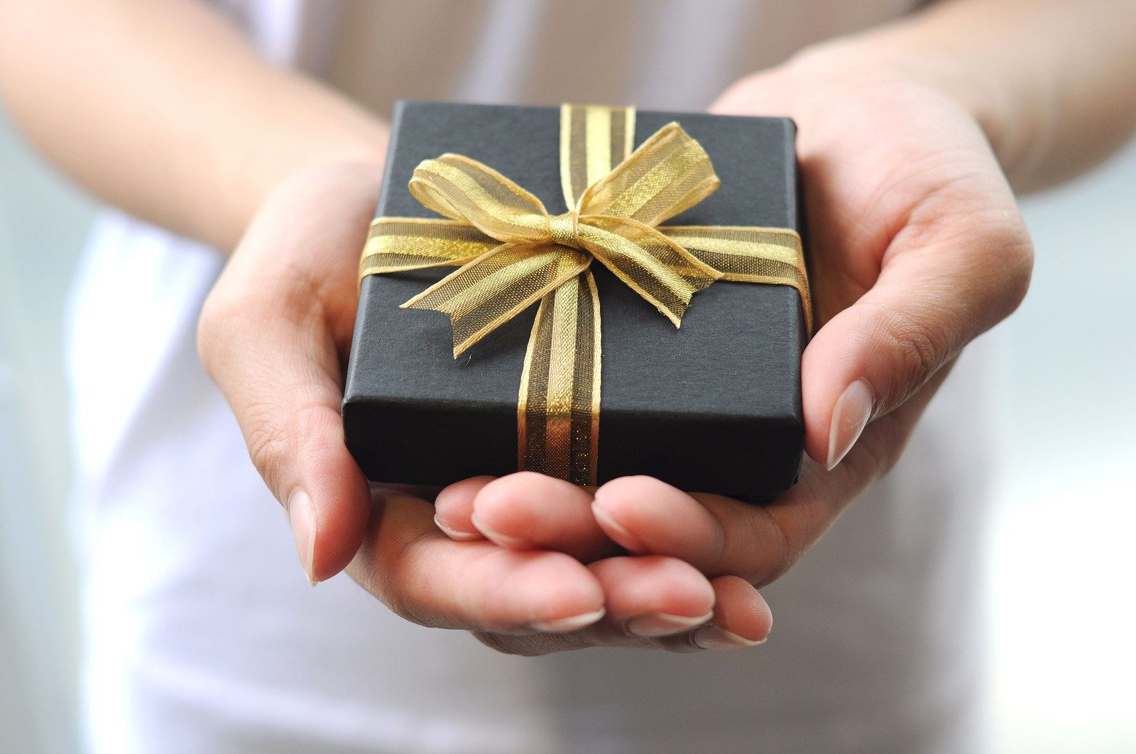Hands presenting a black gift box tied with a gold ribbon