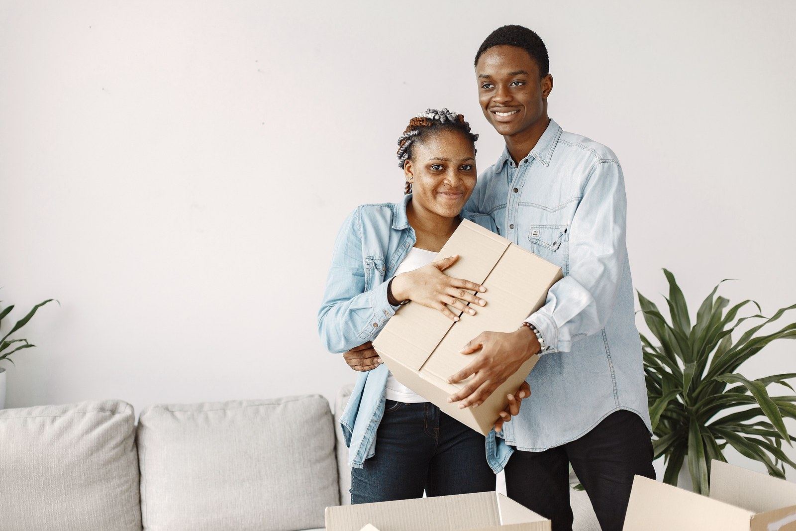 A smiling couple holding a cardboard box in a bright living room