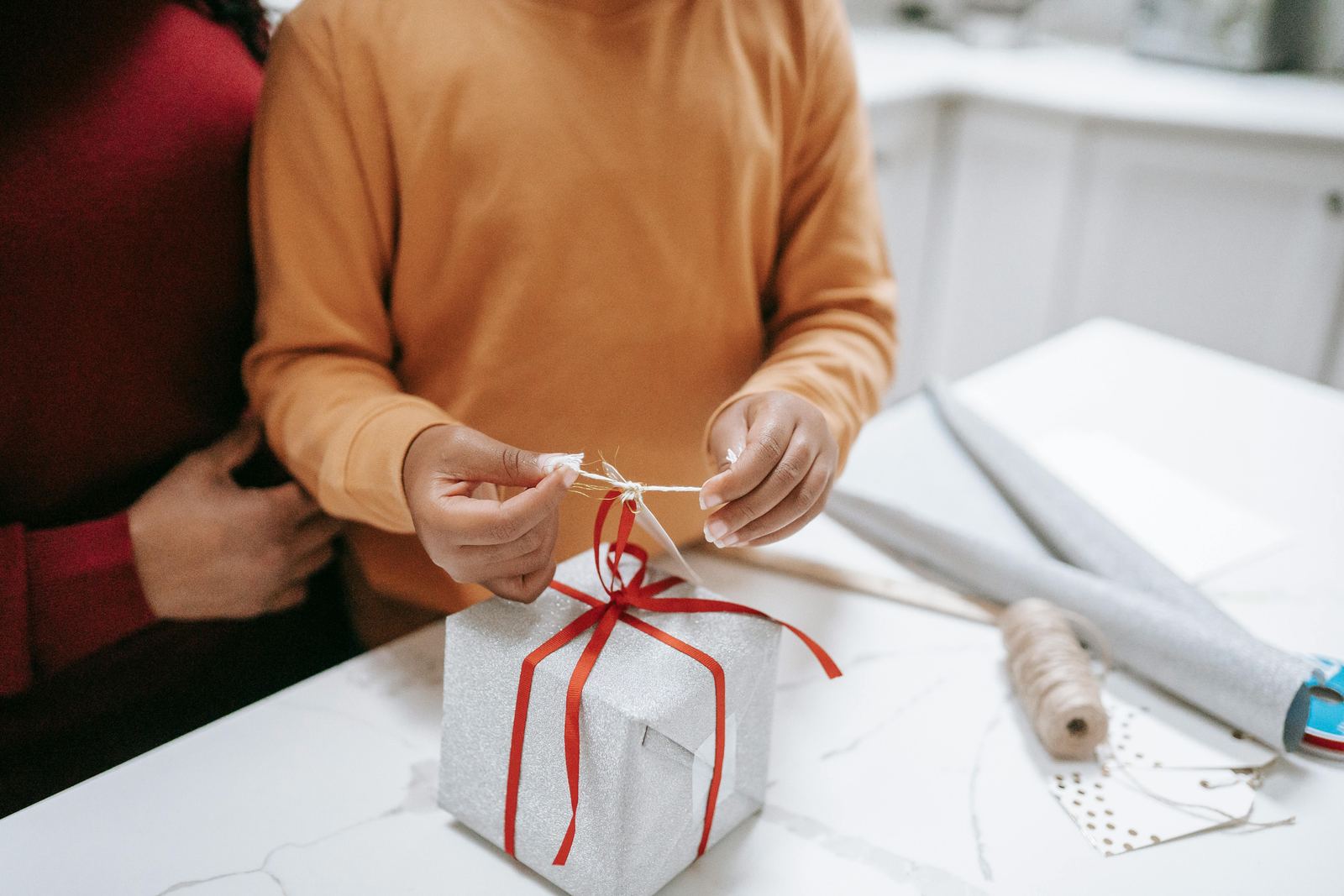 Child wrapping a gift with a red ribbon