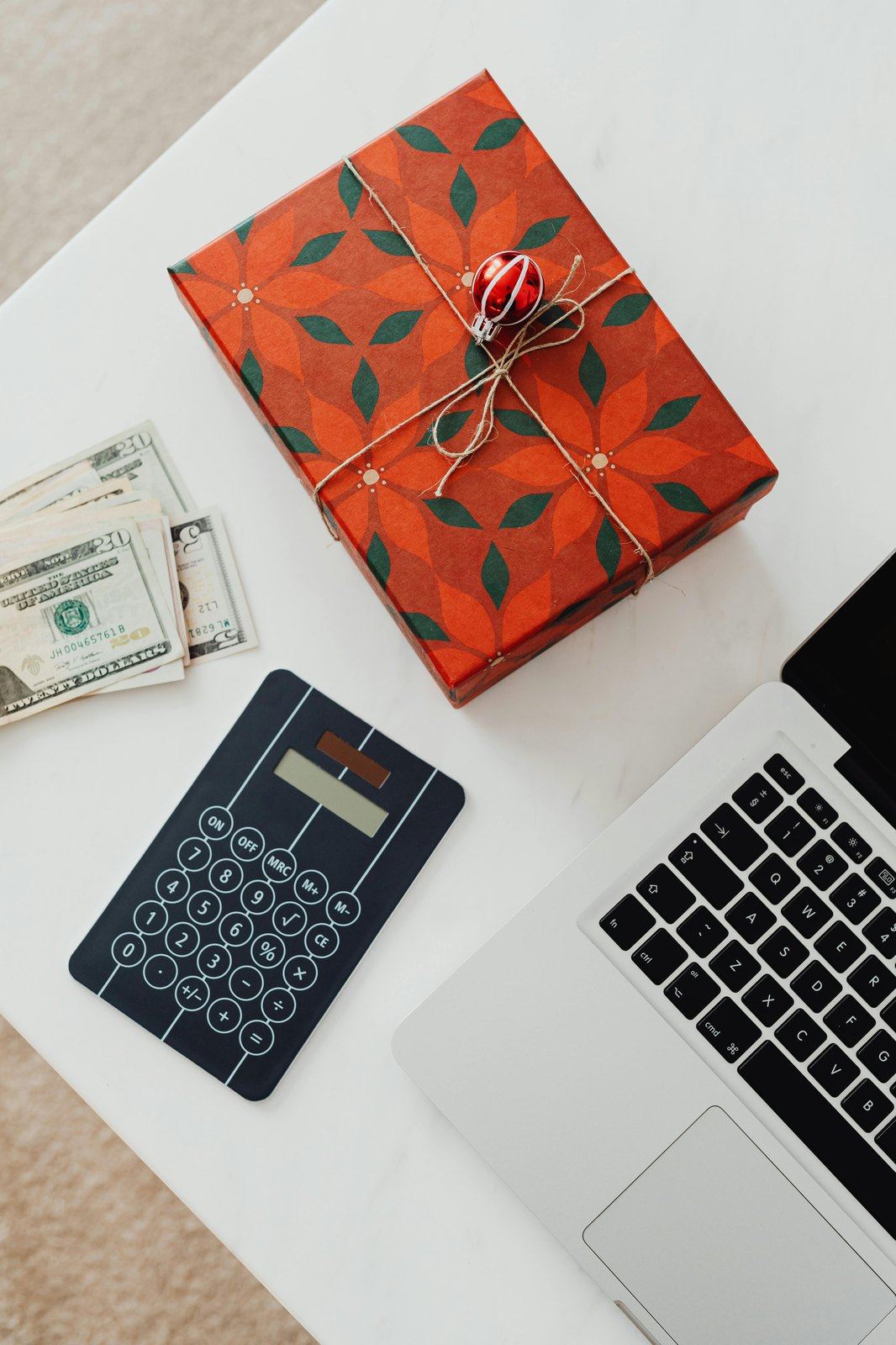 Wrapped gift, calculator, laptop and cash on a white table.