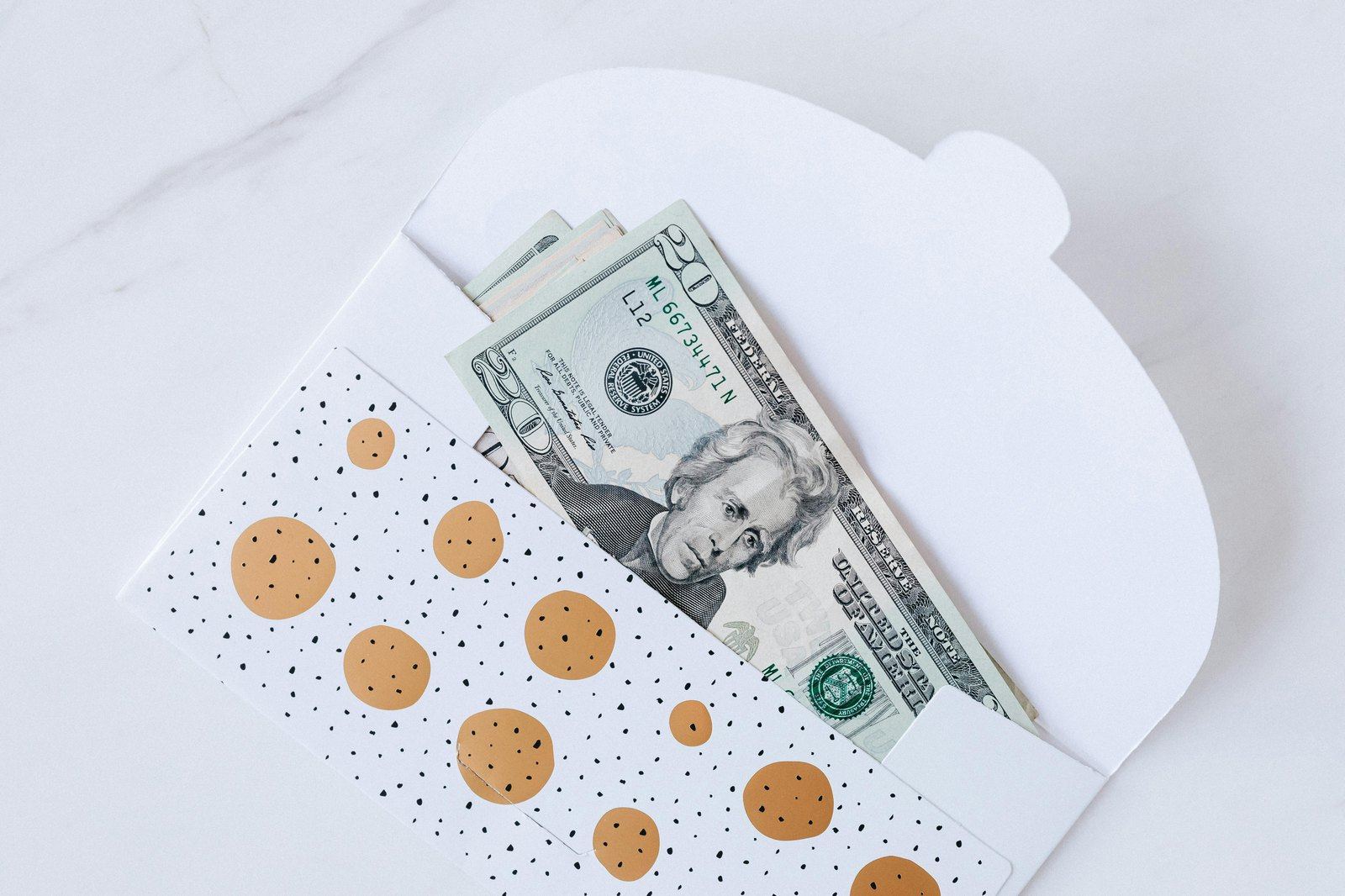Polka dot envelope with cash on a white marble surface.