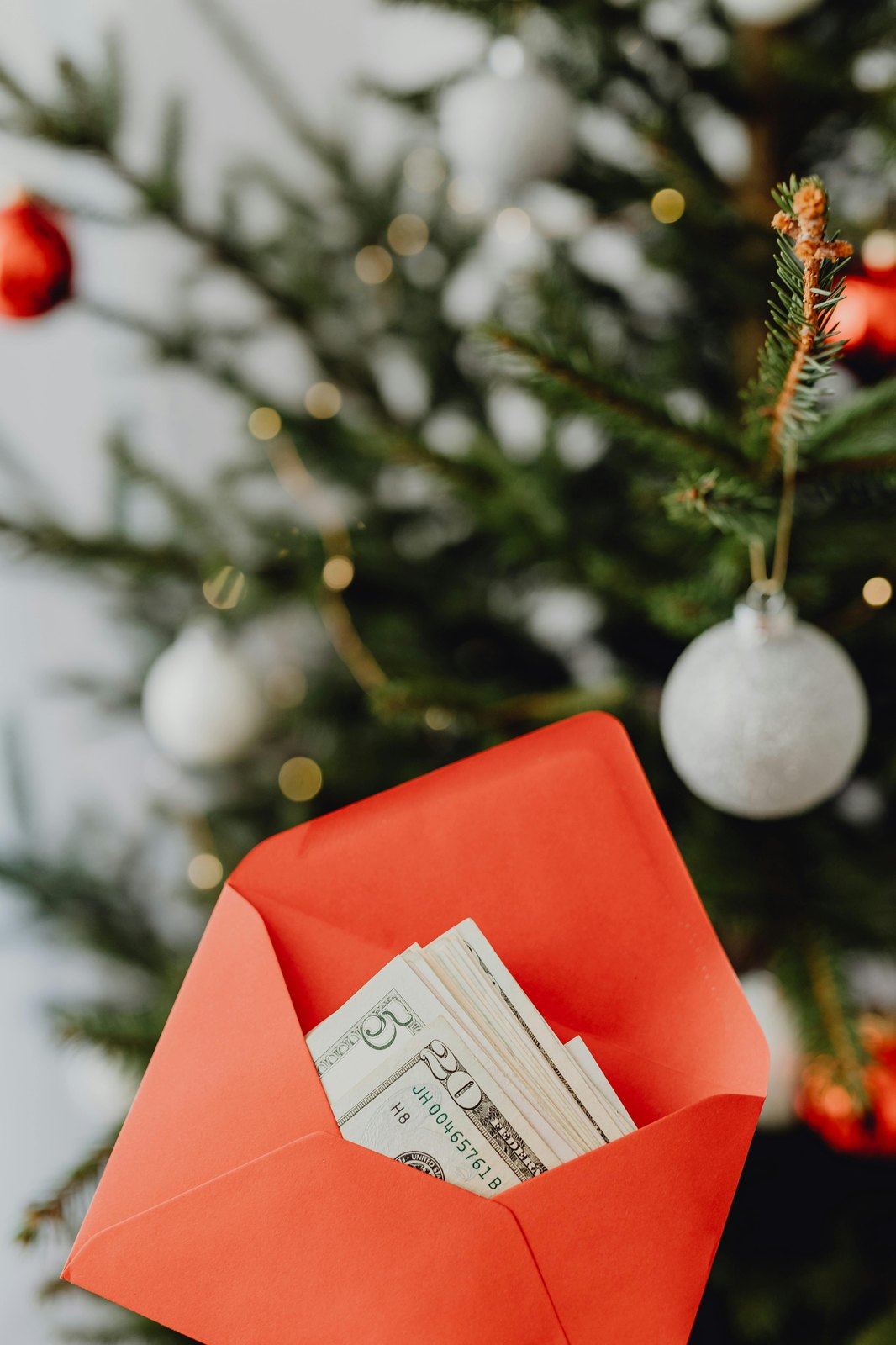 Cash in a red envelope in front of a decorated holiday tree.